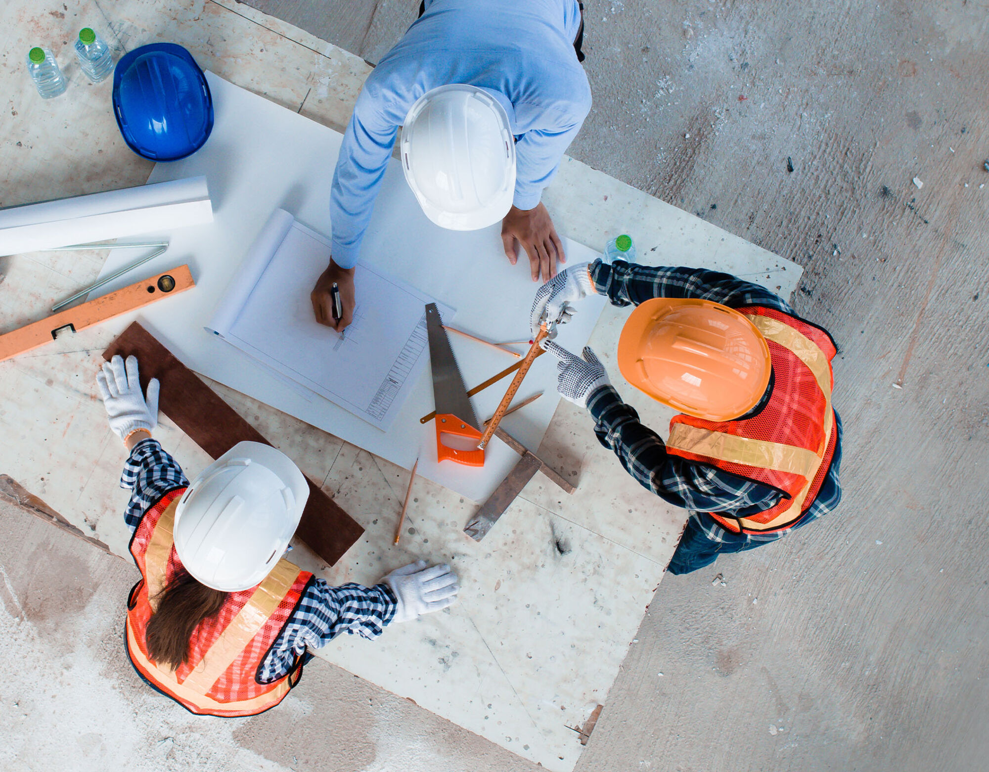 Three construction workers crowd over a notebook and have a discussion that involves using measuring instruments.
