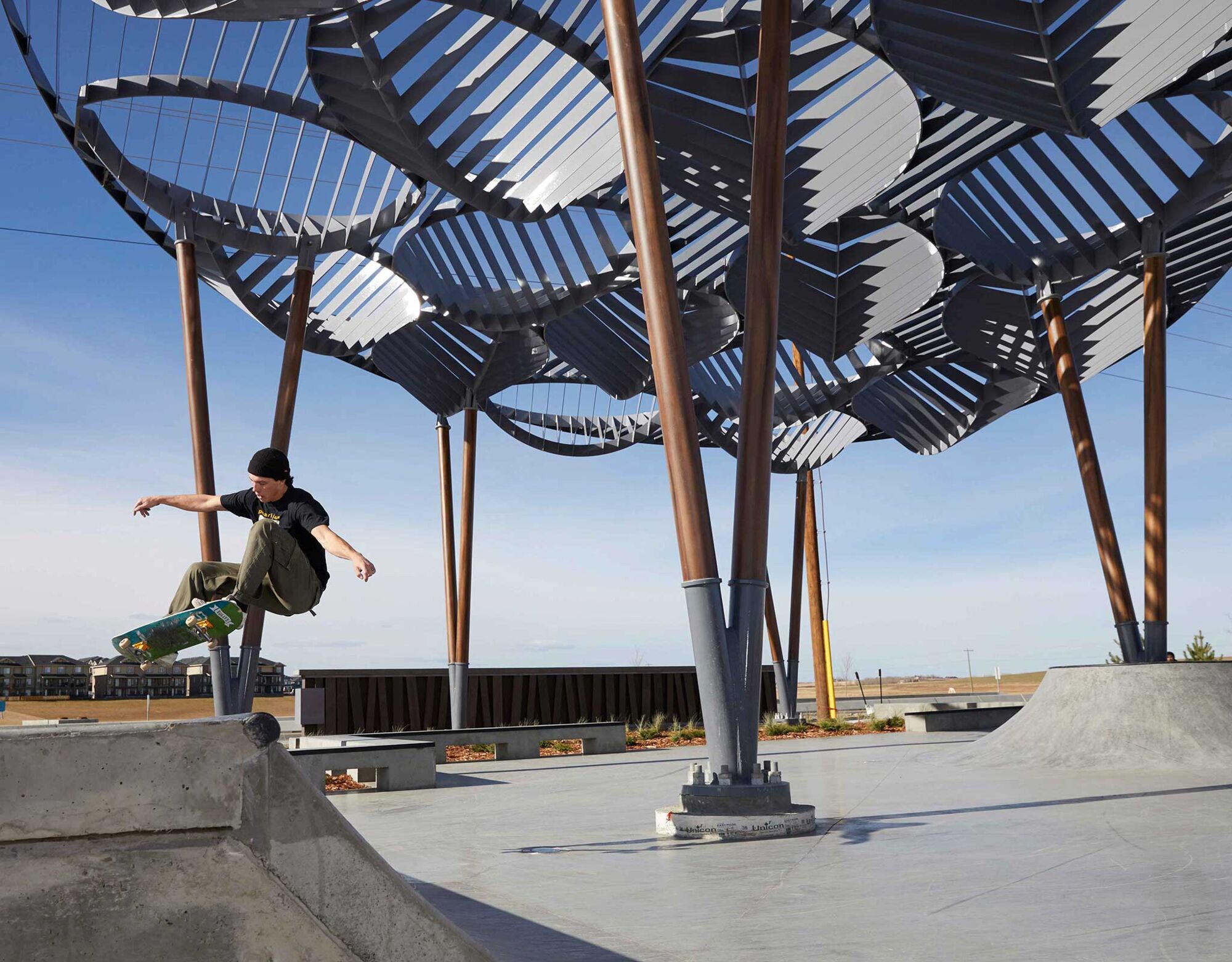 Boy on a skateboard on ramp in a park with large leafy metal designs in the background.