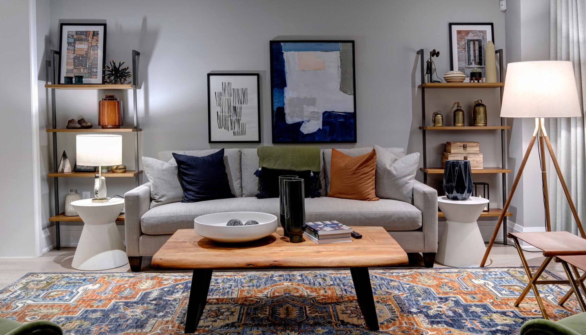 Living room with a grey couch, blue and orange pillows, and a blue and orange rug.