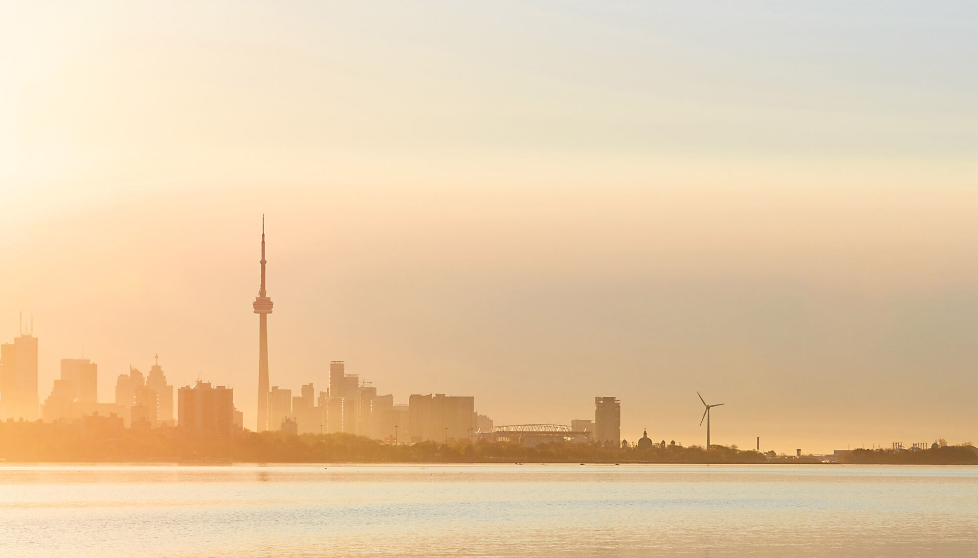 The Toronto skyline right before sunset, producing a golden glow over the skyline and Lake Ontario.