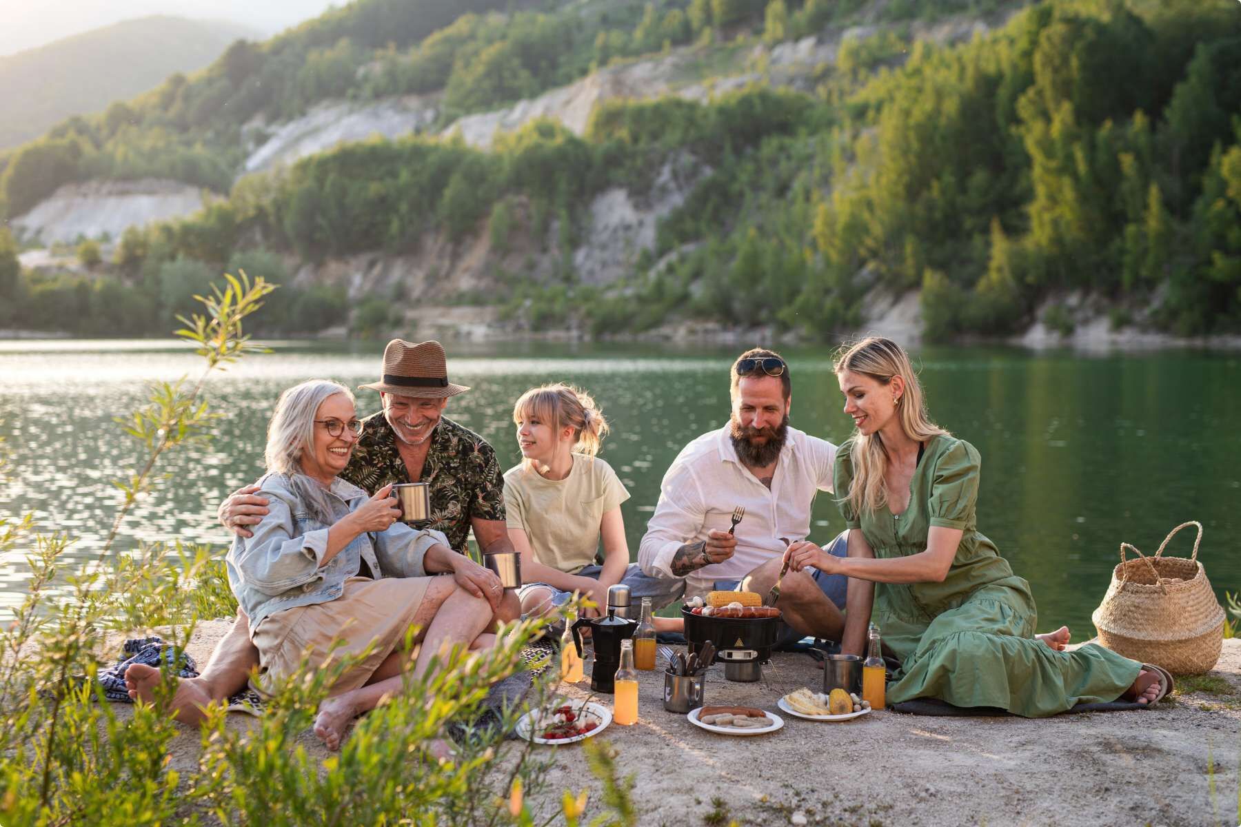 Family of five having a picnic along a lakefront with part of a mountain in the background.