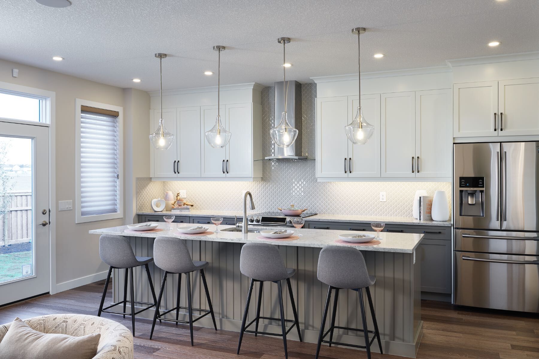 Kitchen with vertical white cabinets and a flat kitchen island with grey barstools. 