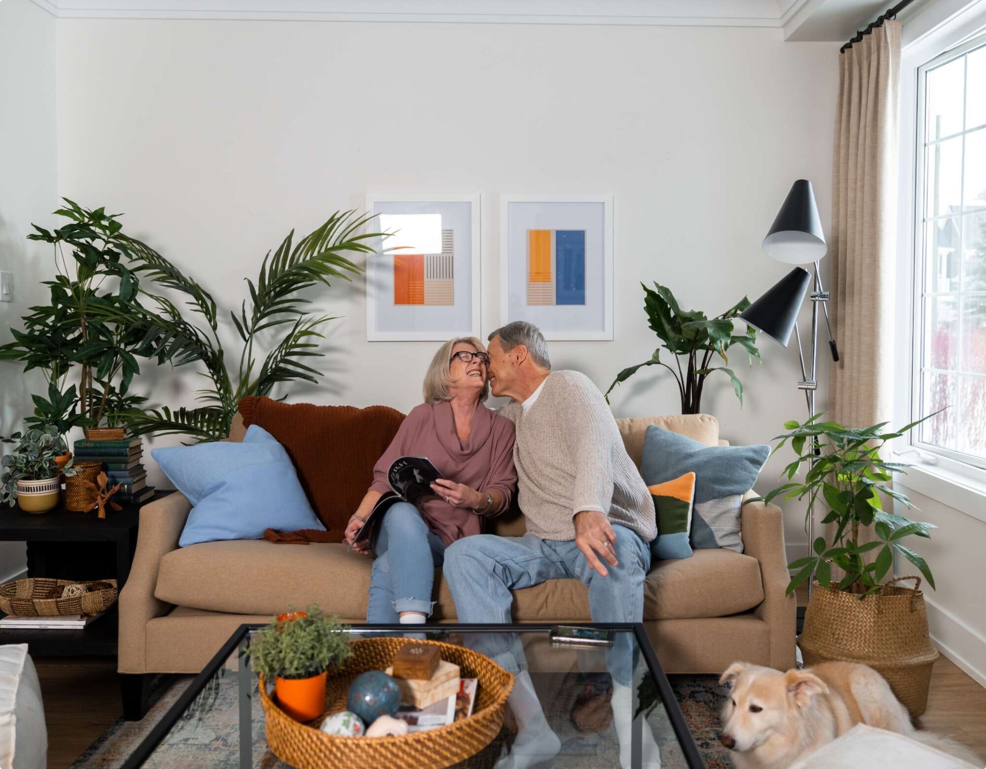 An older couple sitting on a couch lovingly with plans and lighting in the background. 