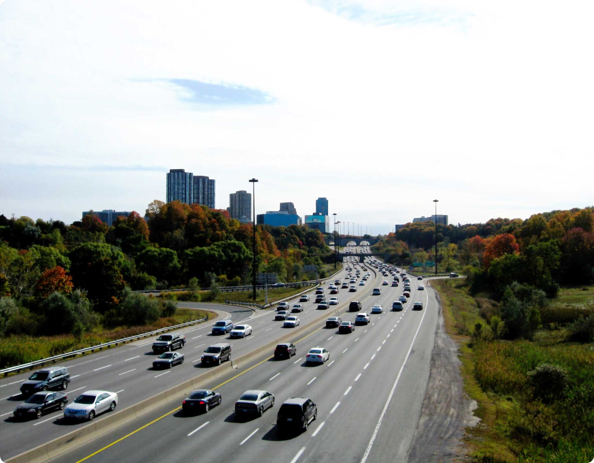 A busy highway with many cars driving past buildings and trees.