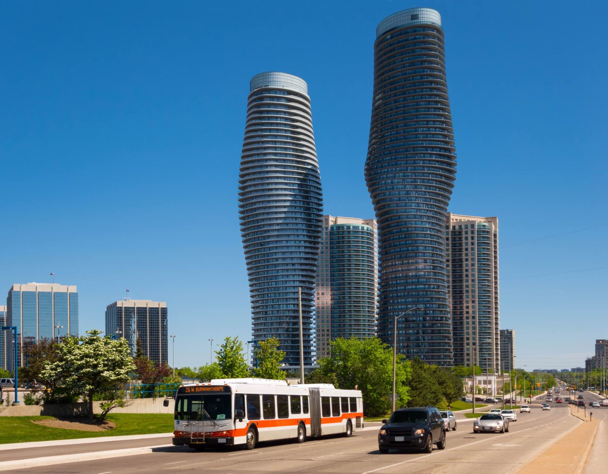 Two coca cola shaped high rise buildings in Mississauga with a bus driving by. 