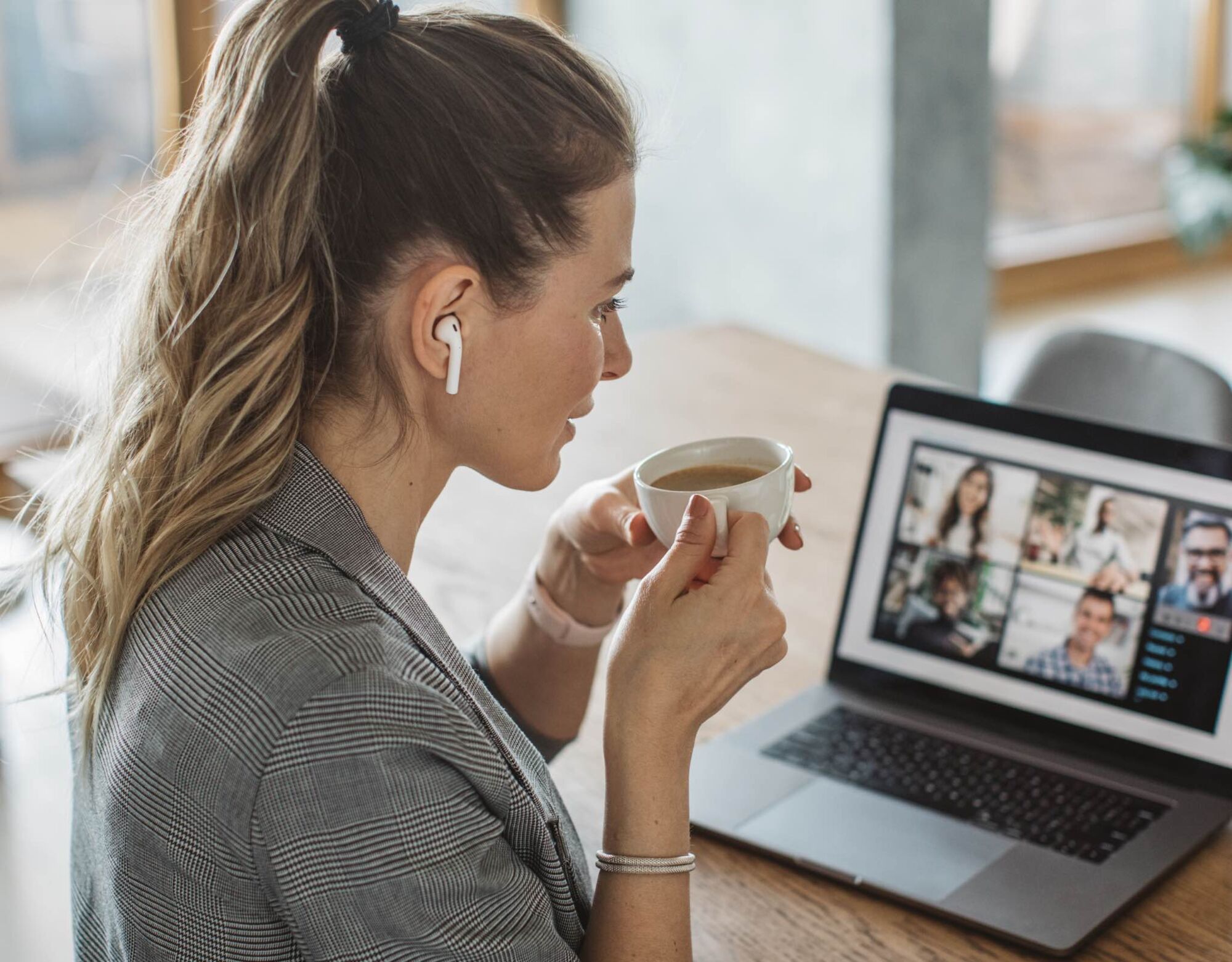 A woman with a coffee cup in her hand while on a virtual meeting on her laptop. 