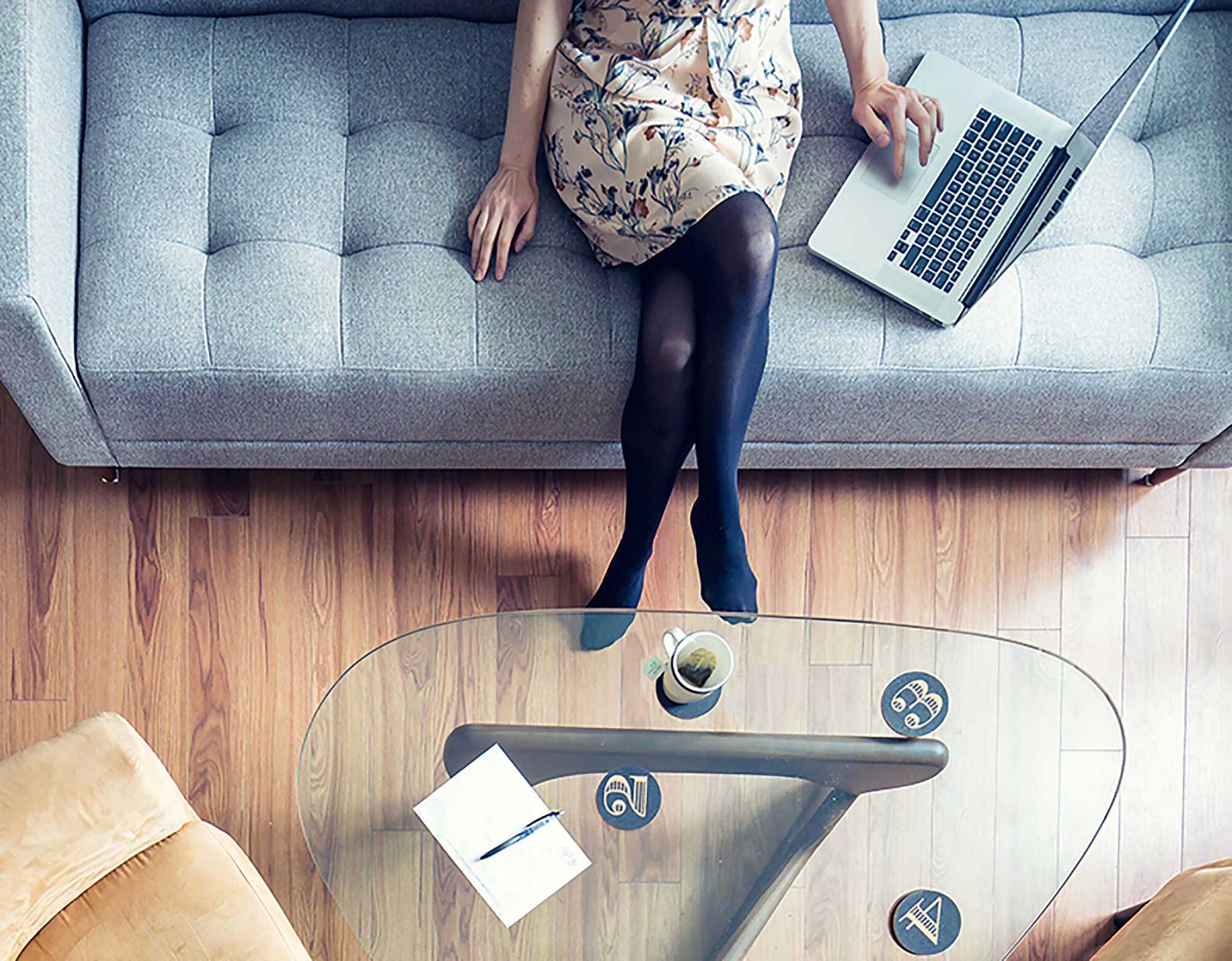 A woman sitting on a couch with her laptop in front of a coffee table with coffee. 