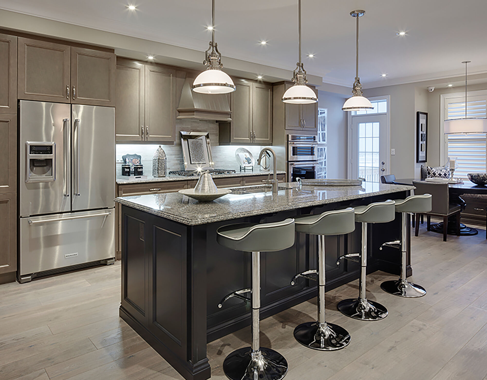 A kitchen with a center island and grey barstools with long pendant lights and light brown cabinets. 