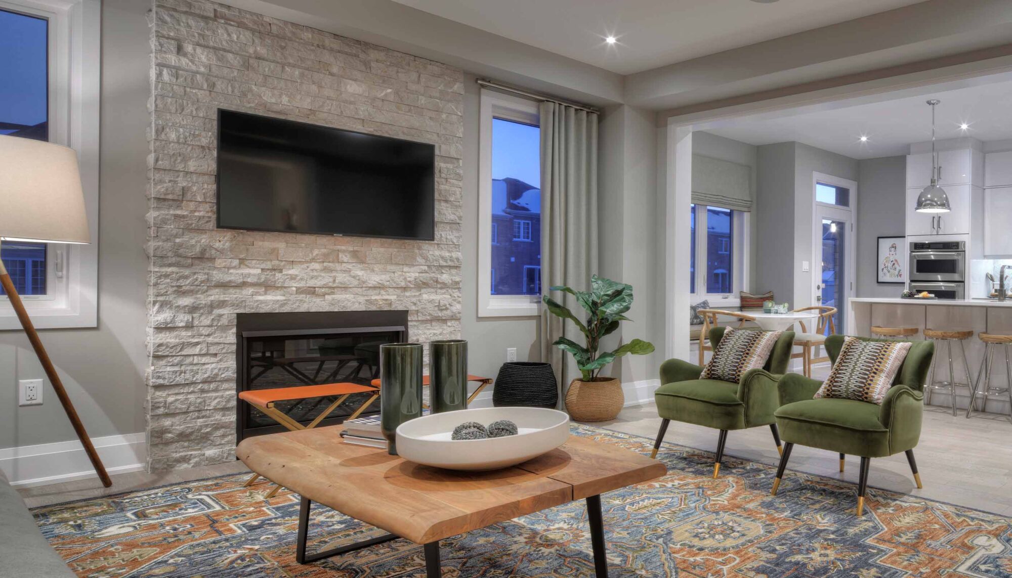 Living room with green armchairs, a blue and orange patterned rug, and a fireplace.