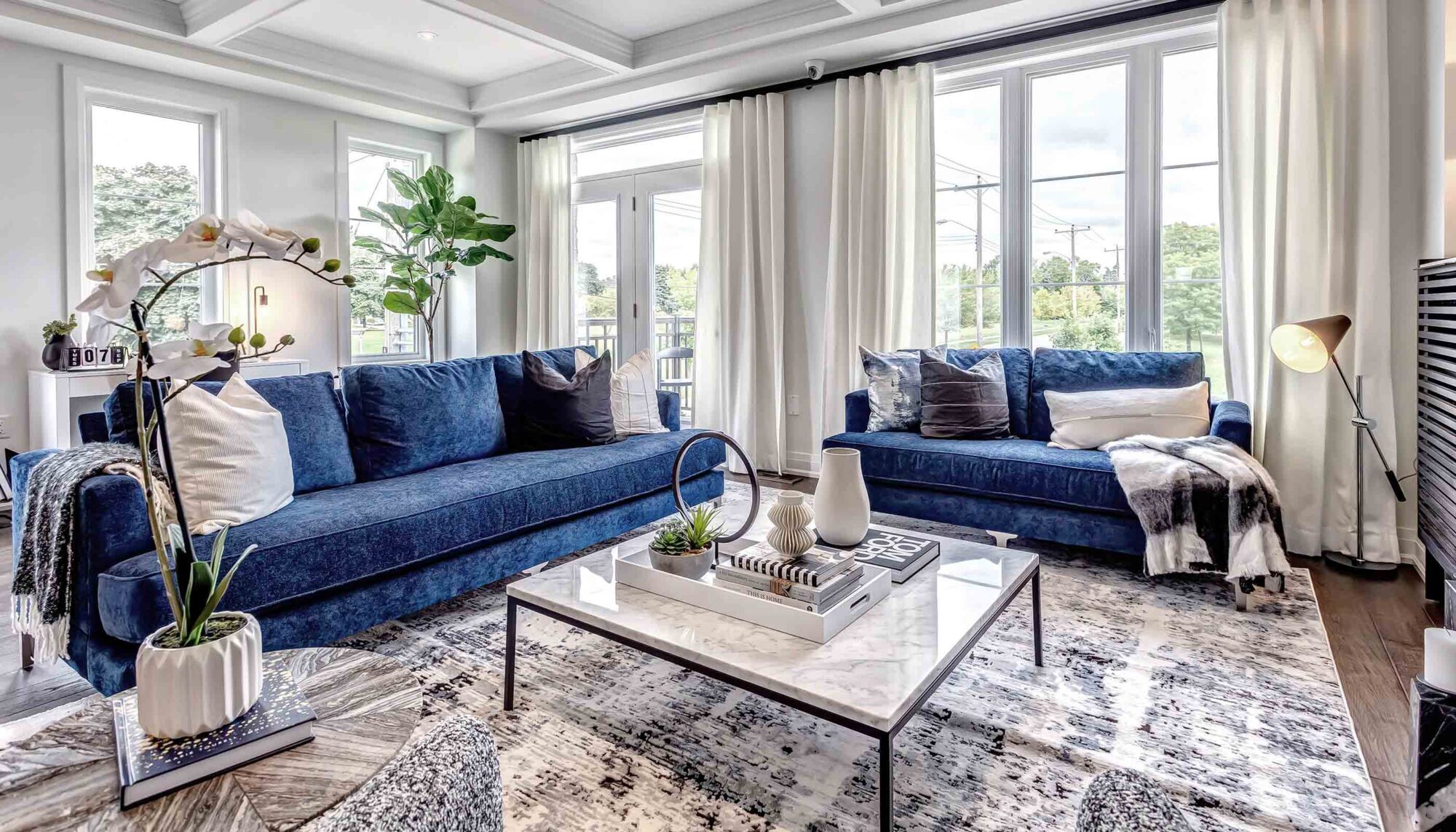 Living room with two blue velvet couches against large windows.