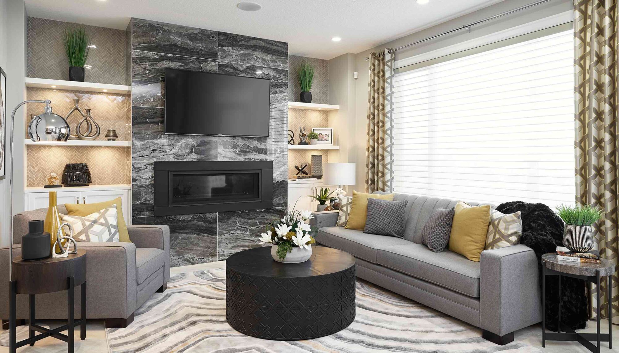 Living room with a grey couch and armchair surrounding a fireplace and television.