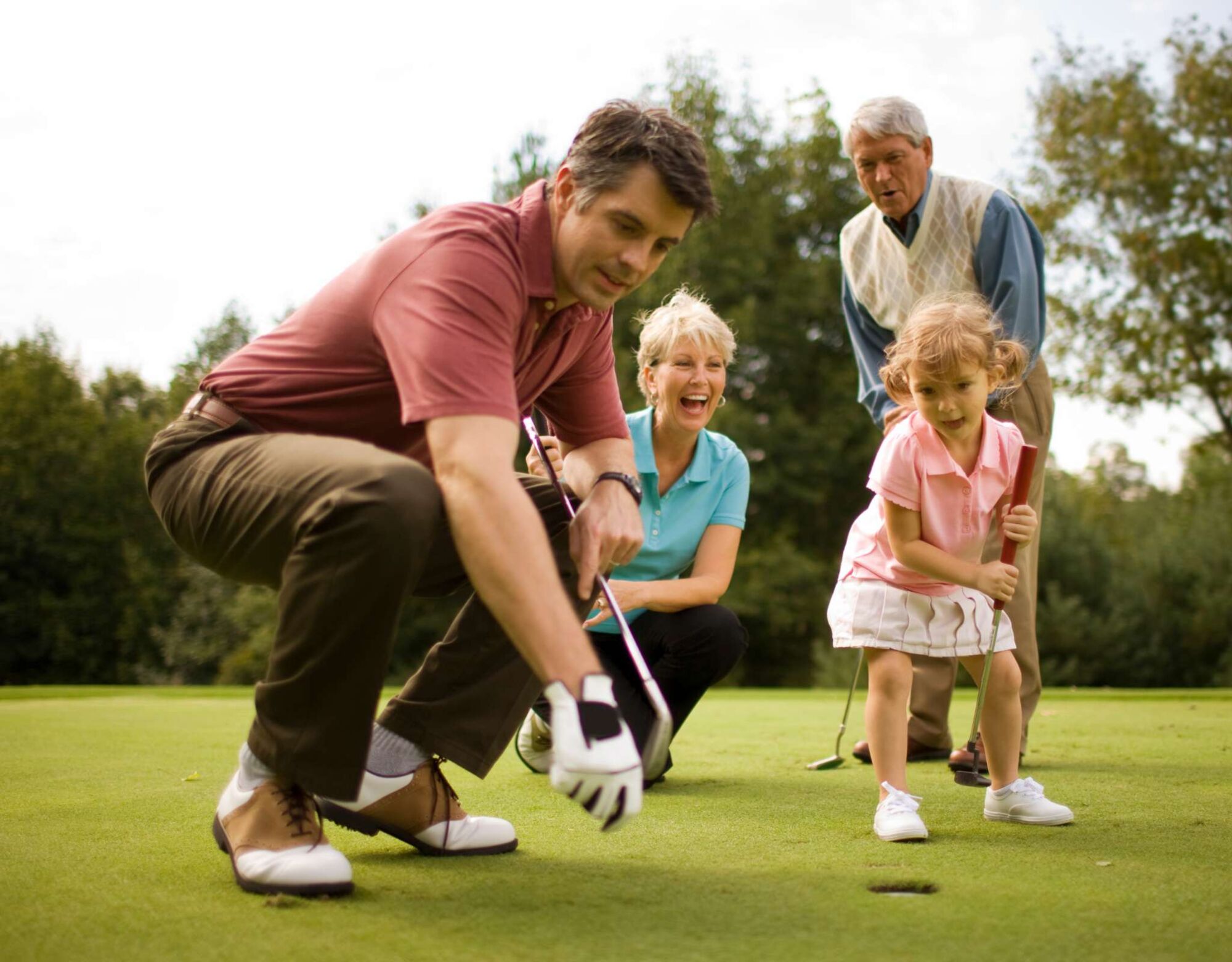 A child plays golf with her mother, father, and grandfather.