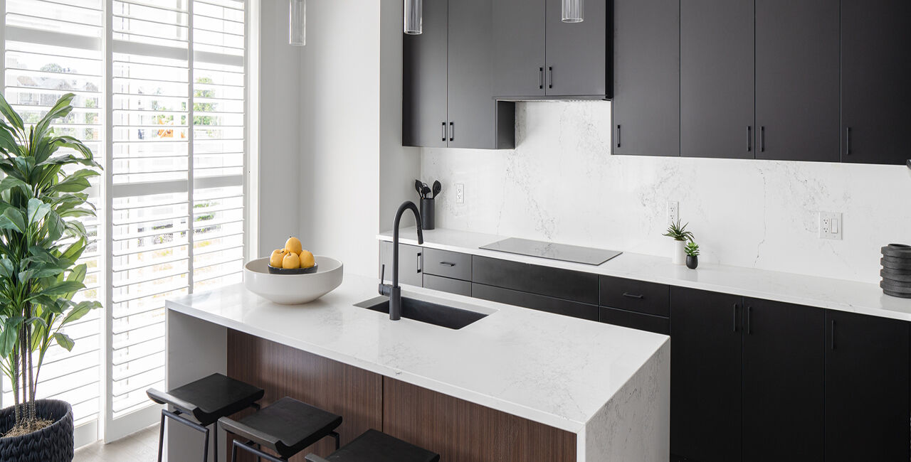 Kitchen with a white marble island, black counter stools, and black cabinets.