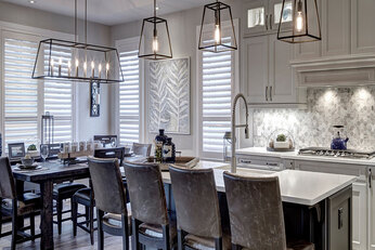Kitchen with center island and grey chairs and the dinning room off in the background with pendants lights. 