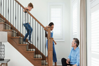 Two children walk down wooden stairs to their father at the bottom.