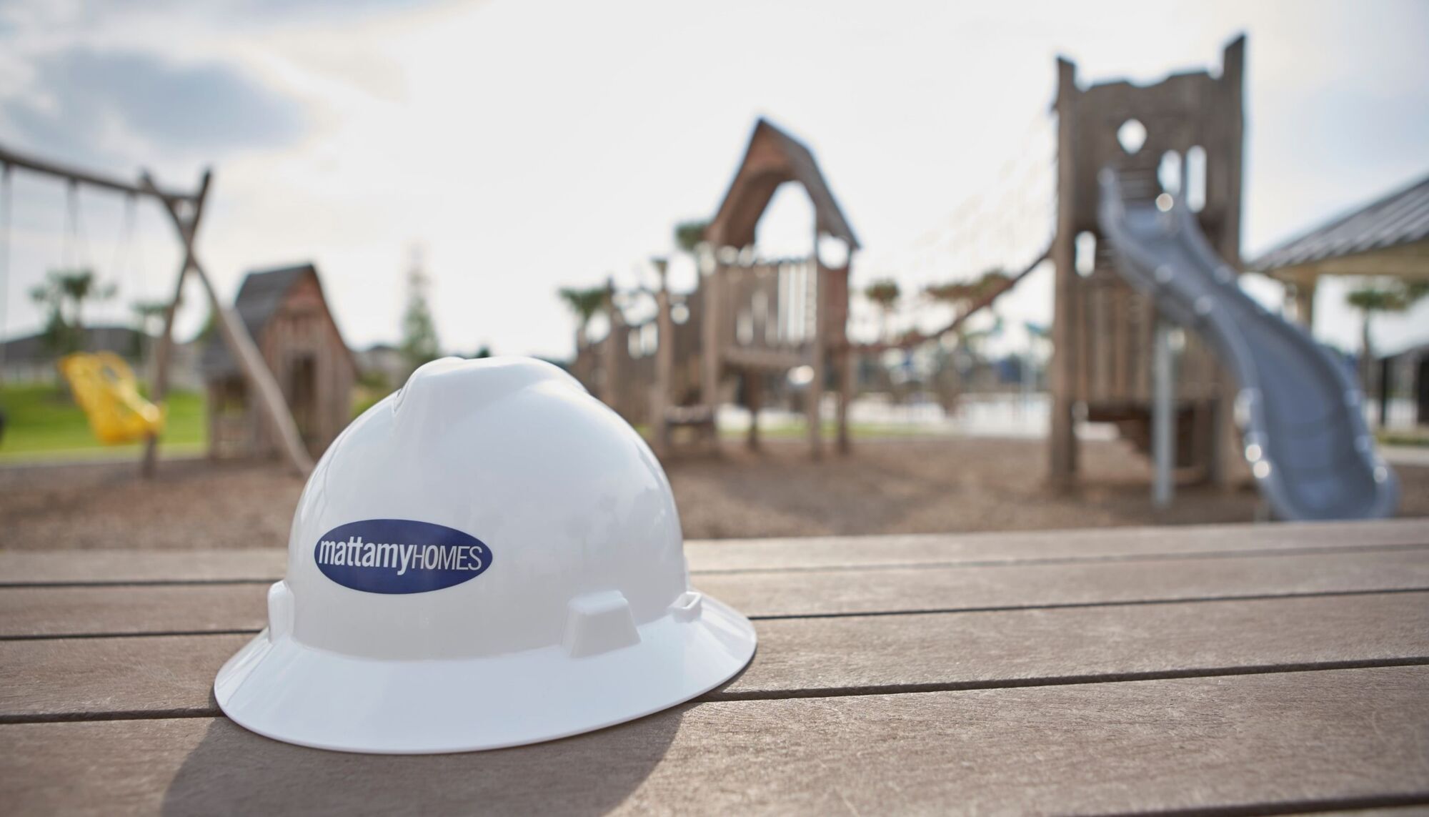 White construction hardhat with Mattamy logo set on picnic table with playground behind it