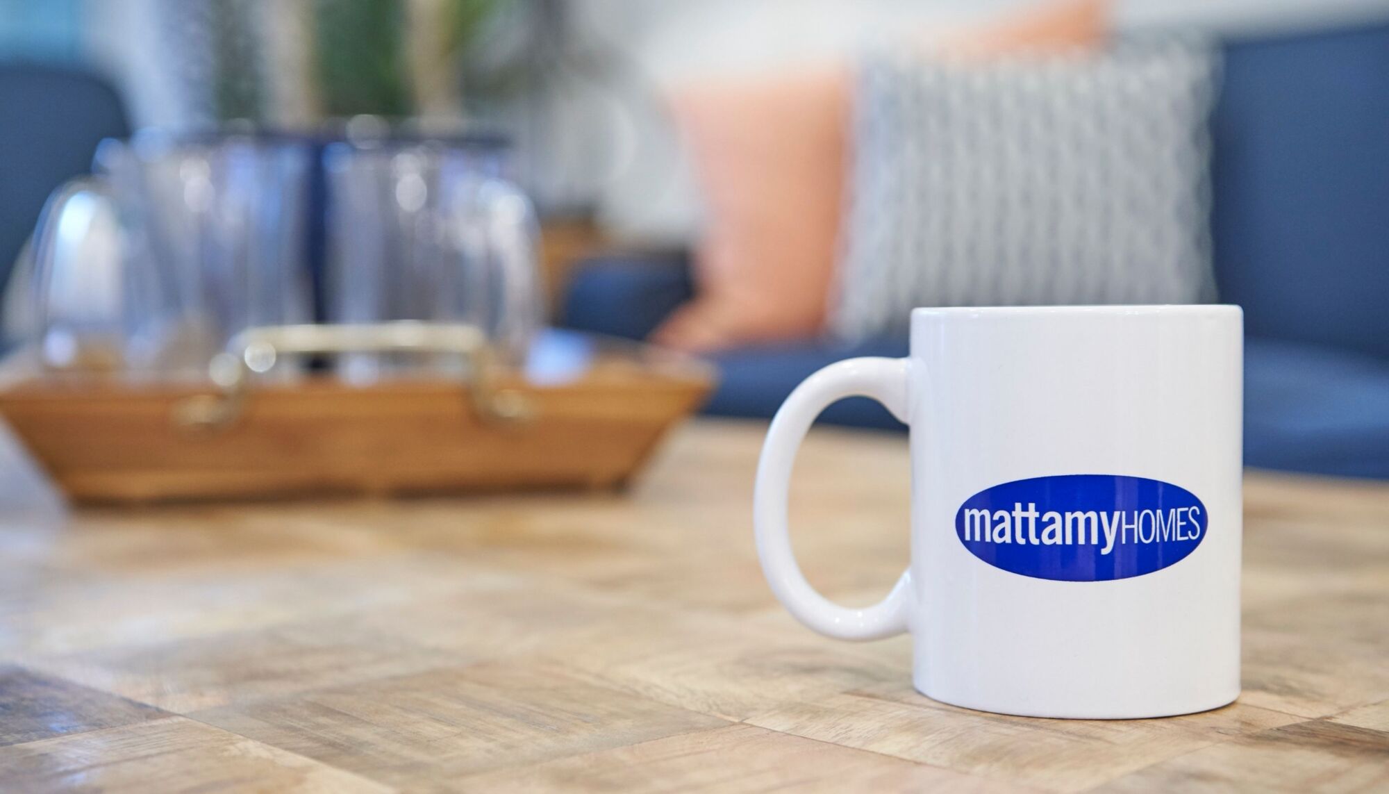 White mug with blue Mattamy Homes logo on it, being displayed on a wooden coffee table