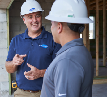 Two males wearing hard hats smiling at one another in a home under construction