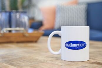 White mug with blue Mattamy Homes logo on it, being displayed on a wooden coffee table