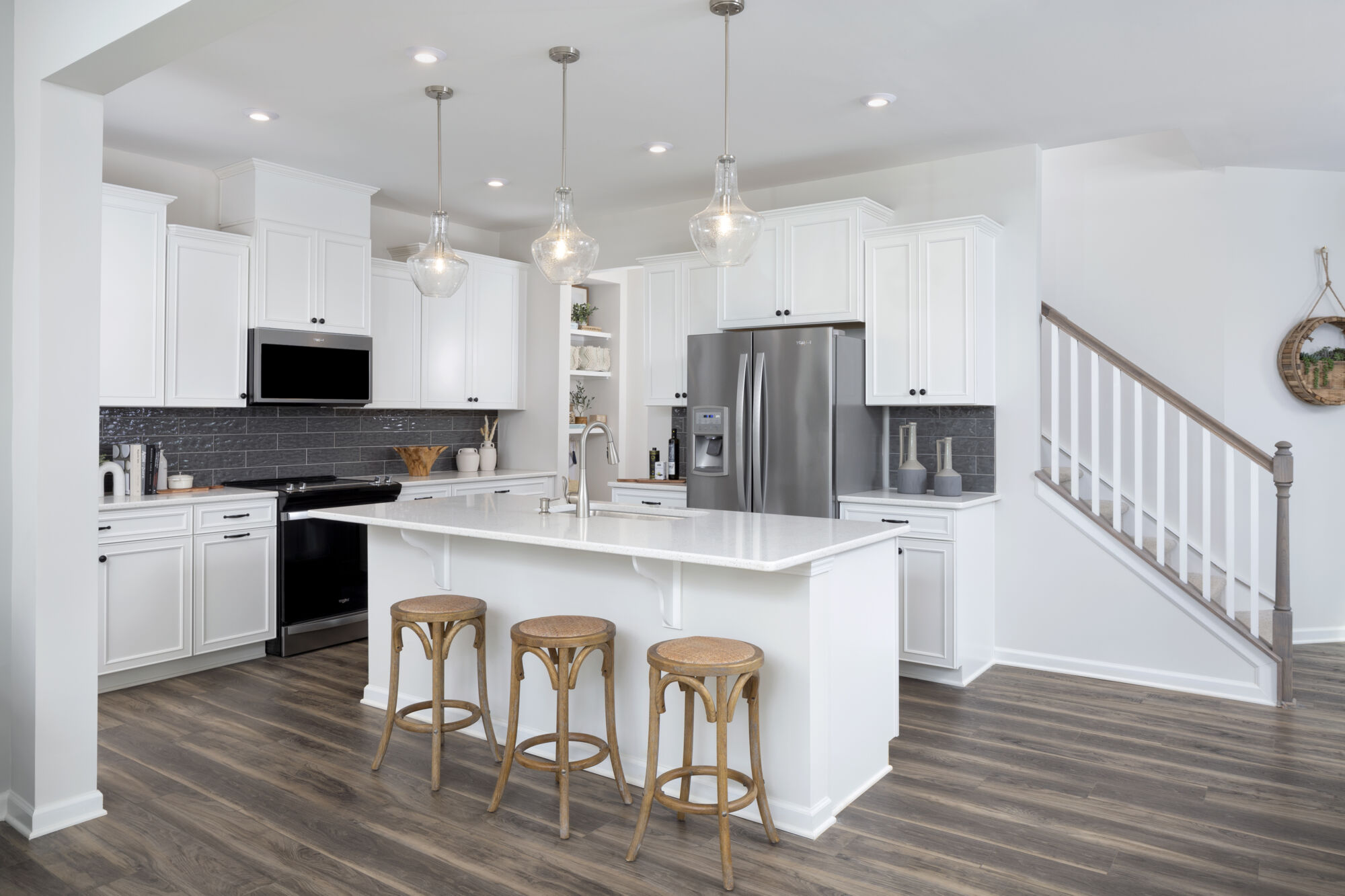 L-Shaped Kitchen with pendant light, refrigerator, white cabinets, range and wood flooring