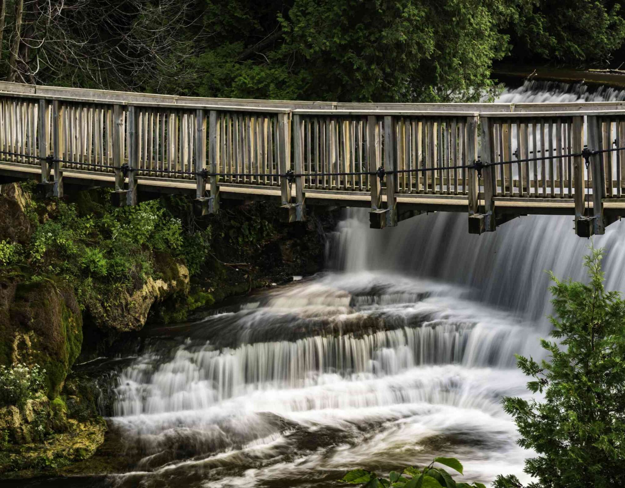A wooden bridge suspended over a small waterfall