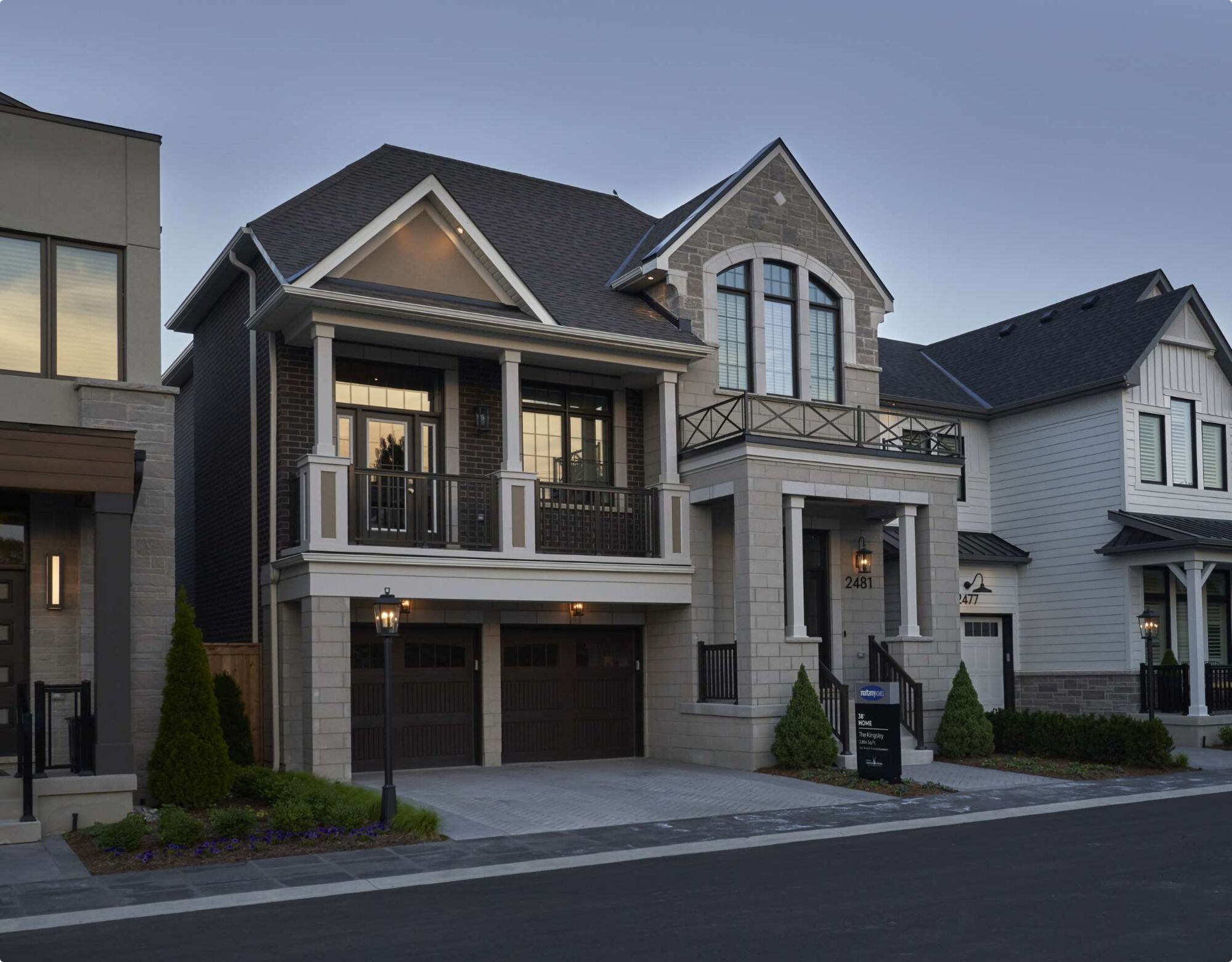 A detached, modern home with a balcony, two-car garage and stone exterior.