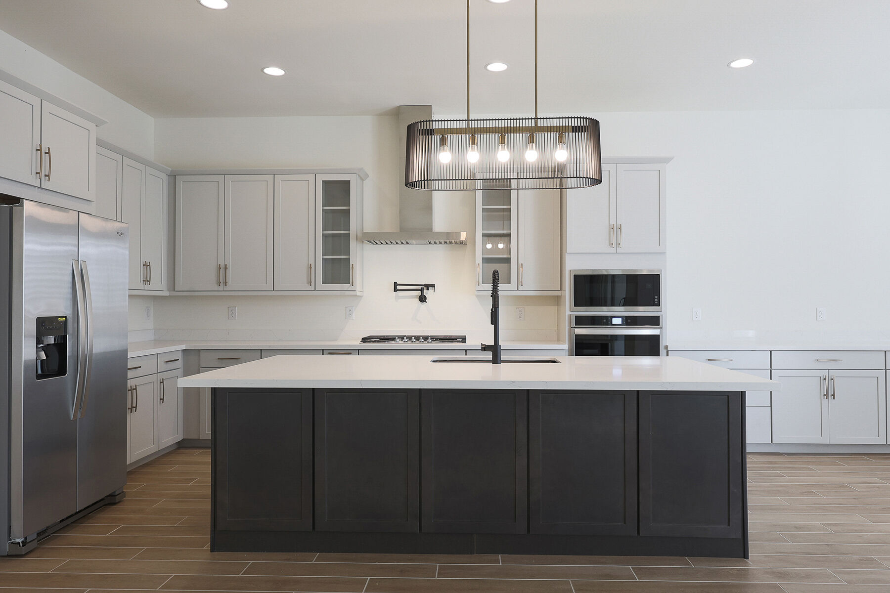 L-Shaped Kitchen with refrigerator, pendant light, cooktop, oven, white cabinets and wood flooring