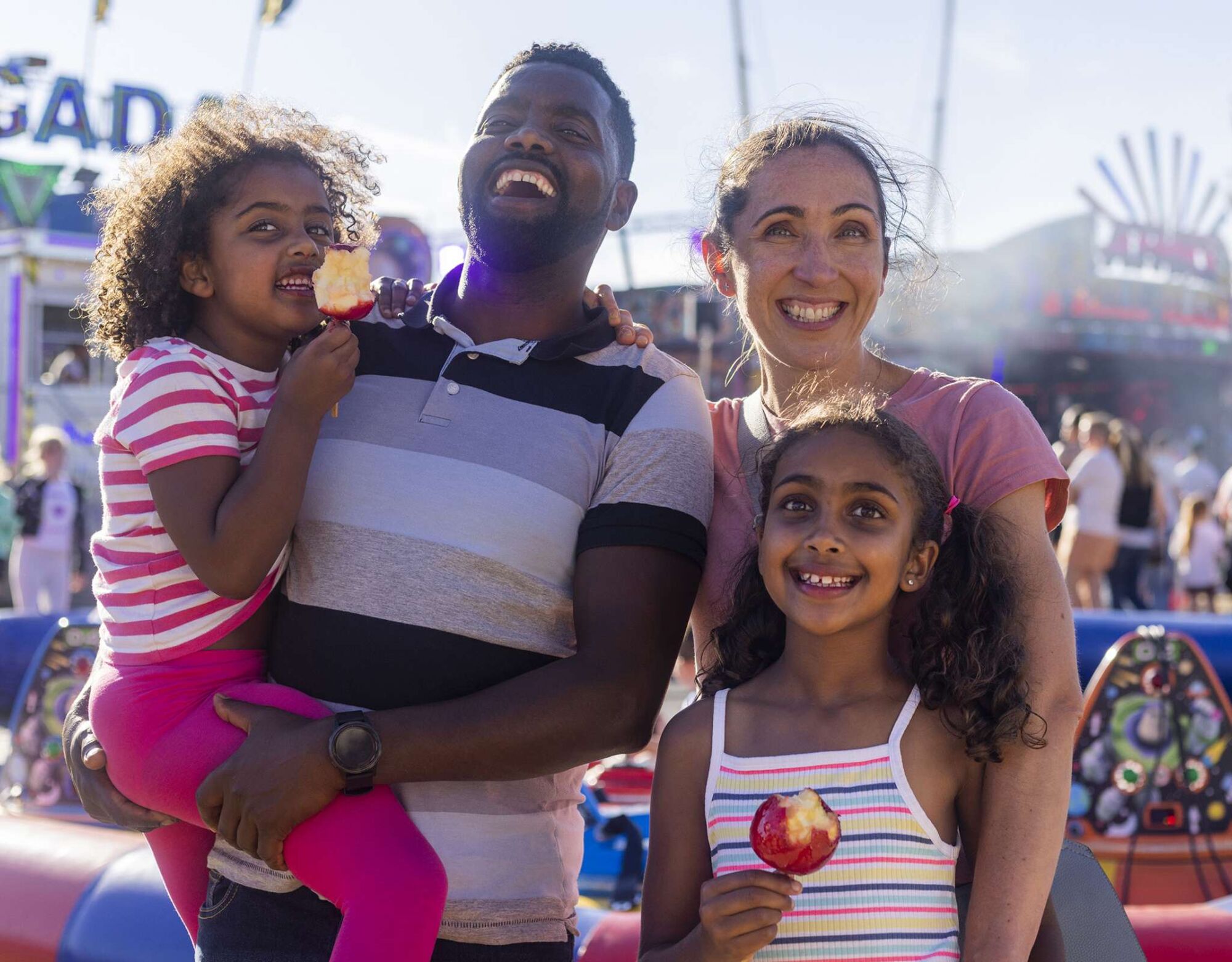 A family of four smiling and eating candy apples at a carnival.