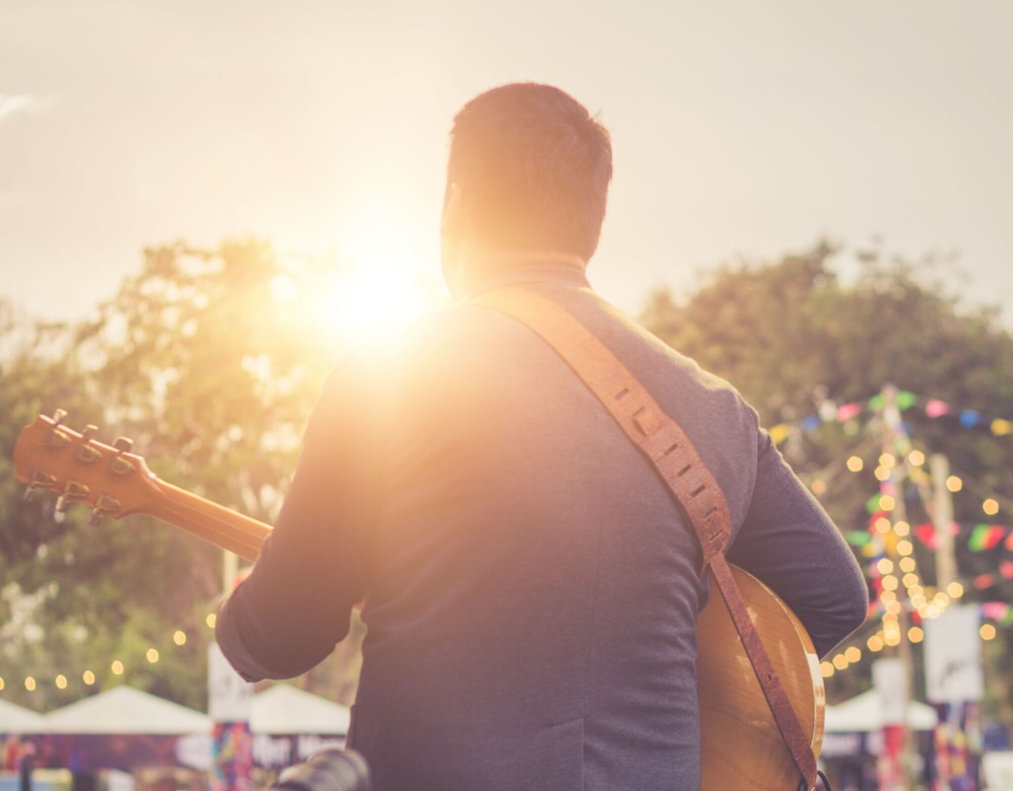 A man playing an acoustic guitar at a festival at sunset.