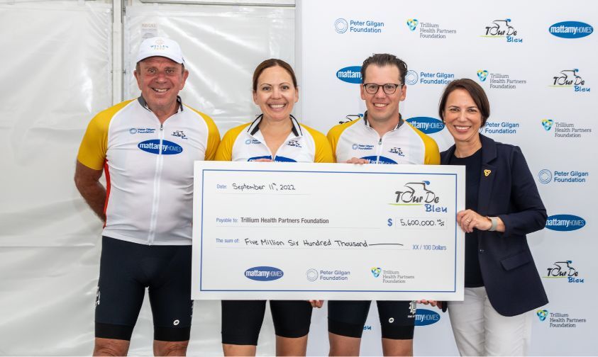 Founder of Mattamy Homes, Peter Gilgan and two other representatives from Mattamy wearing cycling clothing while presenting a large check for $5.6 million to Trillium Health Partners Foundation's CEO.