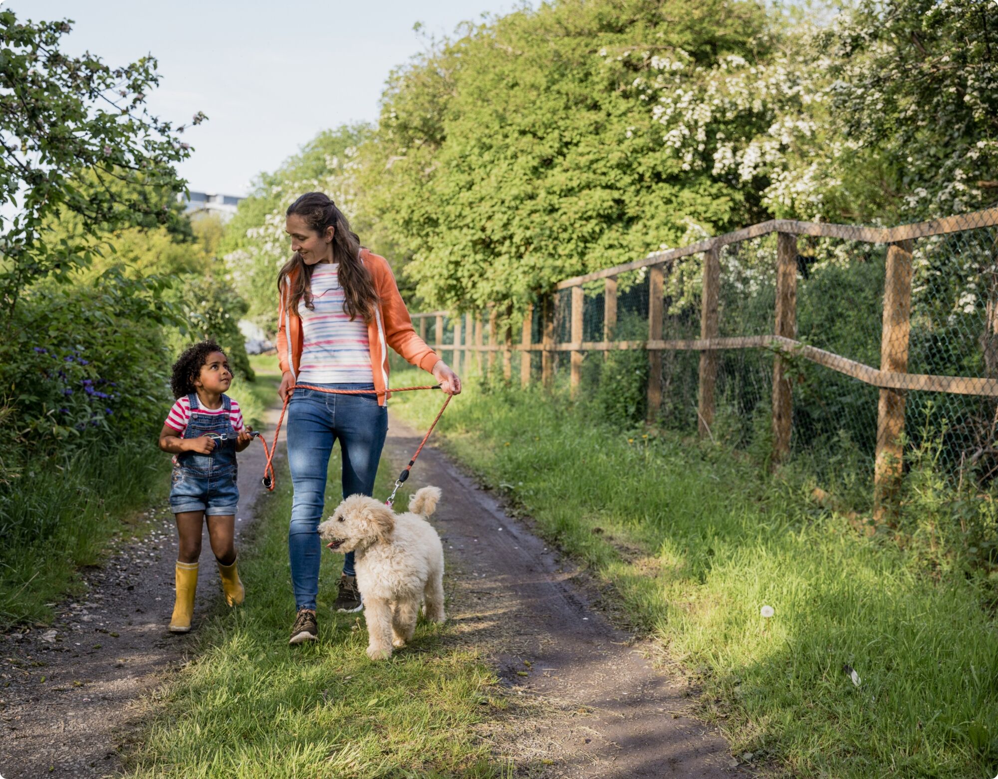A mother and a daughter walking their dog on a country road