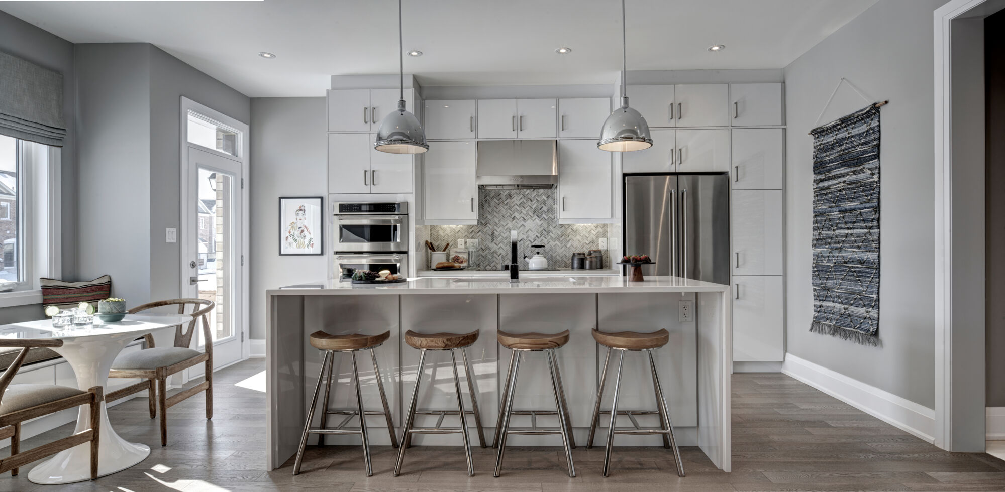 Wide shot of white kitchen, with breakfast nook and backyard door on left, and kitchen with kitchen island in center