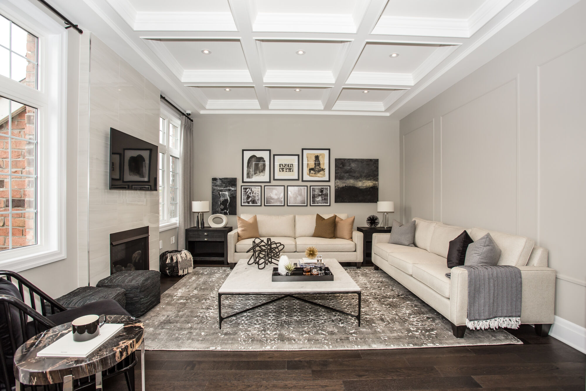 Living room with coffered ceiling, light walls, dark wood floors, double windows with tiled fireplace and mounted tv on the left