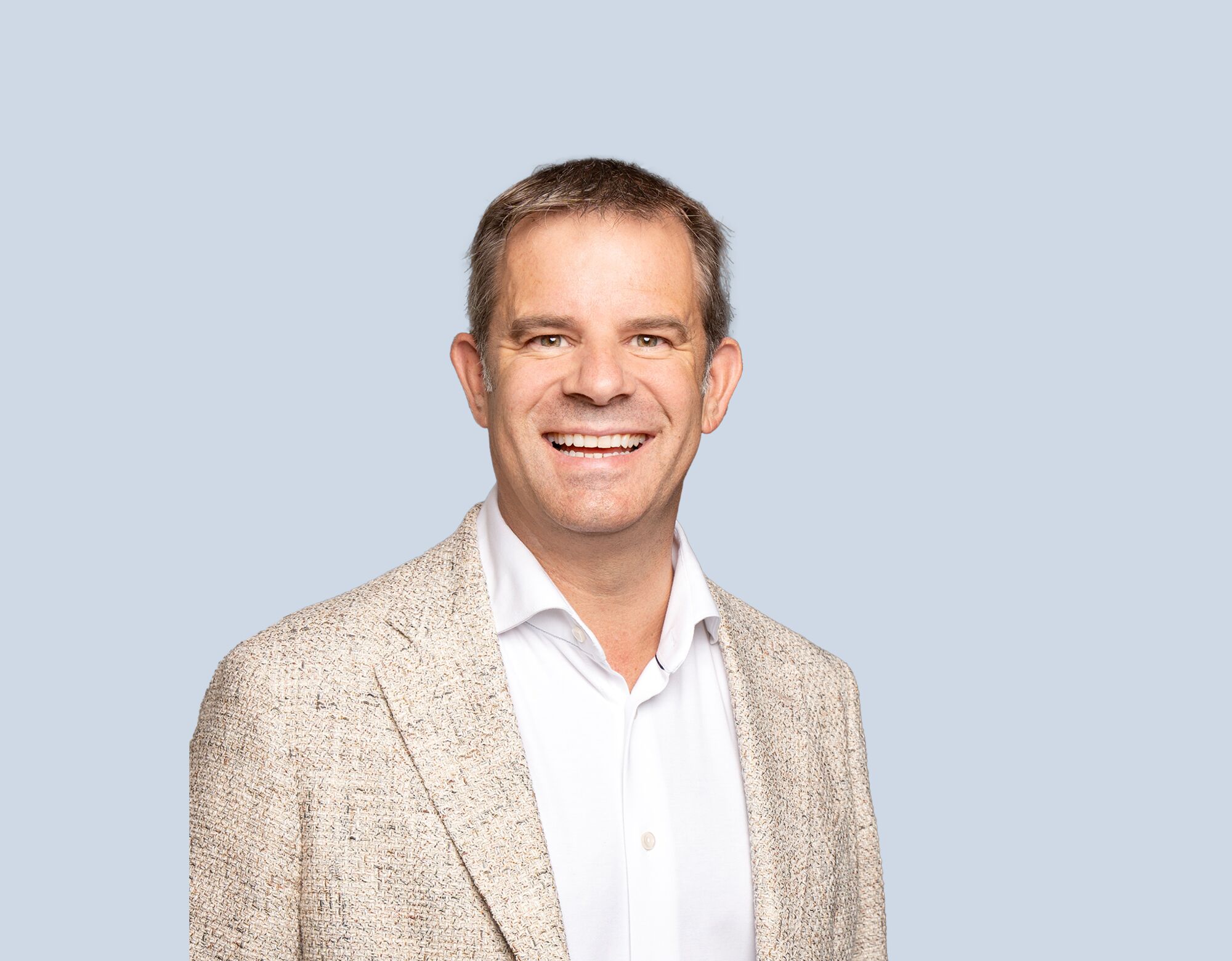 Brad Carr, member of Mattamy Asset Management's Board of Directors, wearing a tan blazer and smiling in front of a blue background