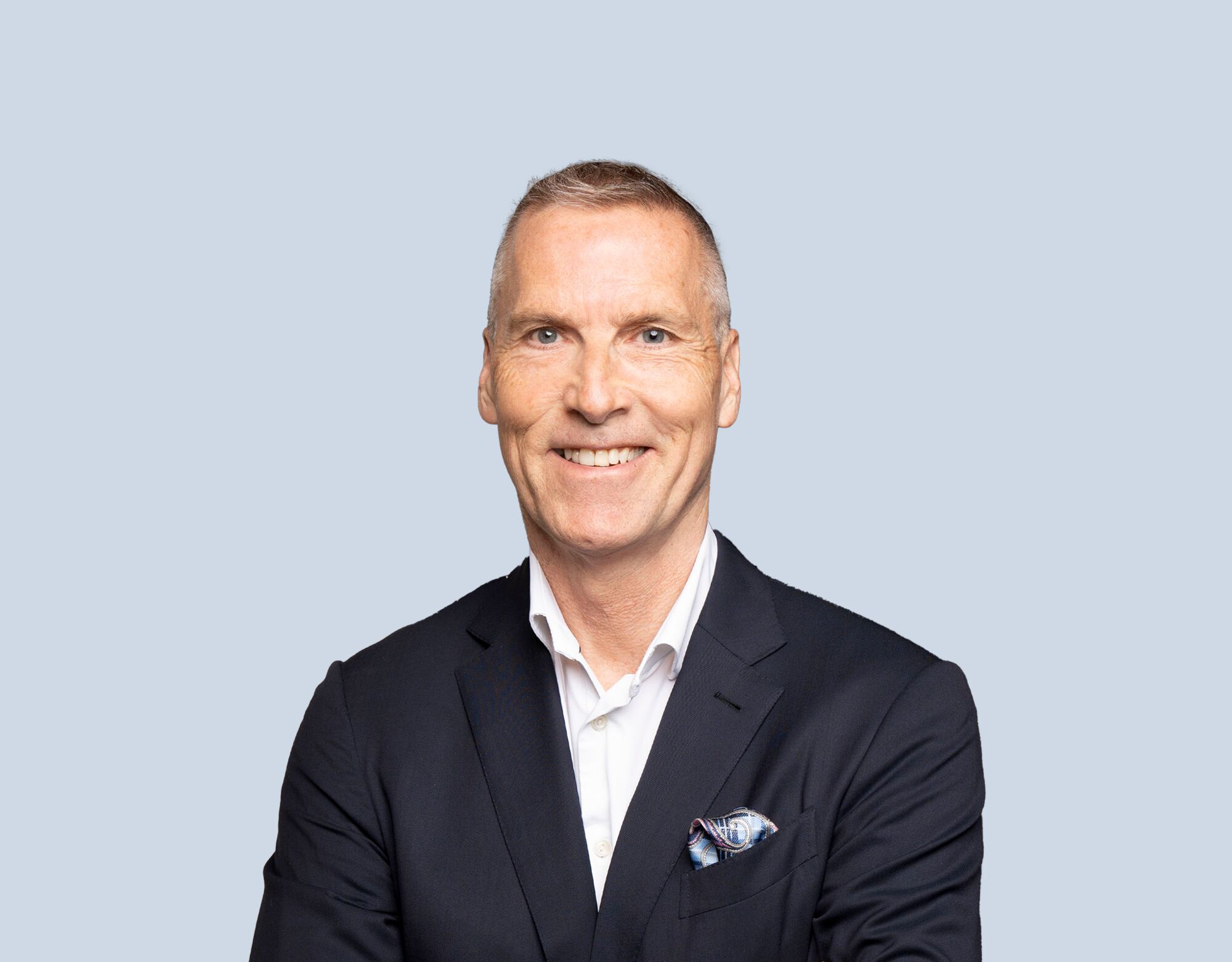 Tim Hockey, member of Mattamy Asset Management's Board of Directors, wearing a dark blue blazer and smiling in front of a light blue background