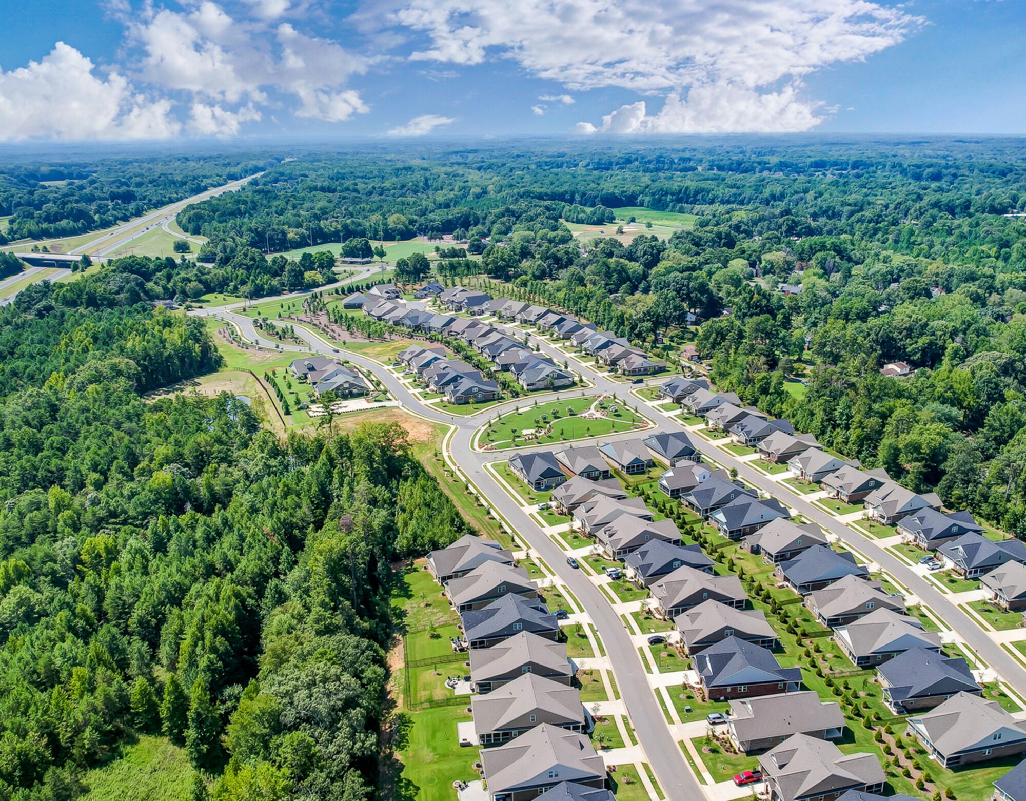 Aerial photo of homes and park in an established Charlotte, North Carolina community surrounded by trees, clouds and blue sky