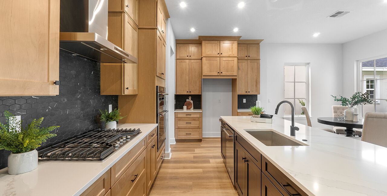 Kitchen with light wood cabinets, dark grey backsplash, white walls and black faucet sink