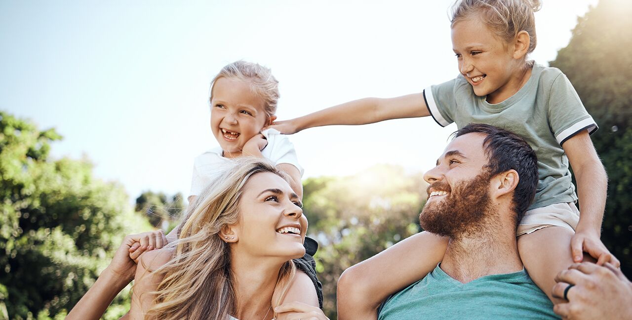 Mom and Dad outside with daughters sitting on their shoulders looking up at each other and laughing