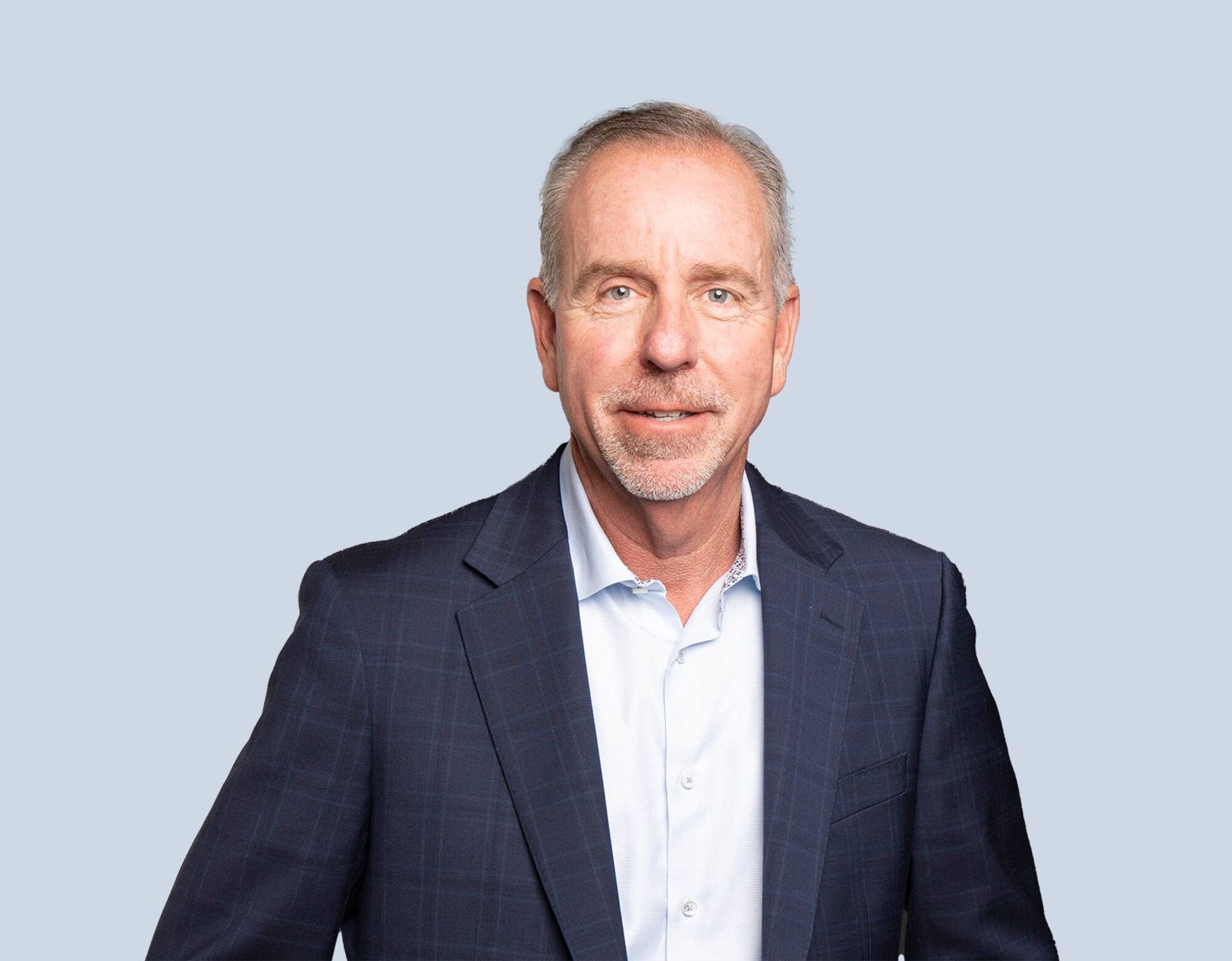 Keith Bass, member of Mattamy Asset Management's Board of Directors, wearing a dark blue plaid blazer and smiling in front of a light blue background