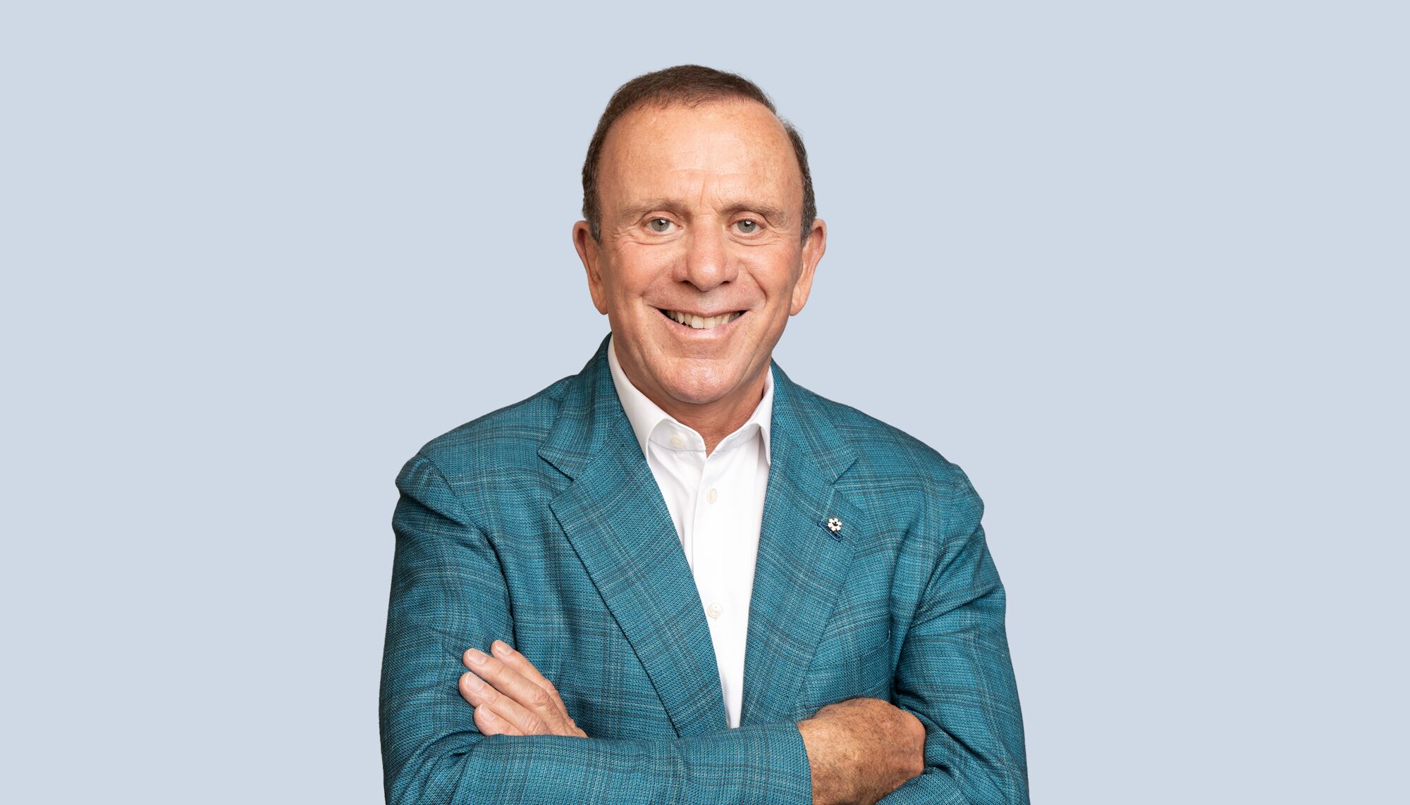   Peter Gilgan wearing a blue suit and white collared shirt in front of light blue background