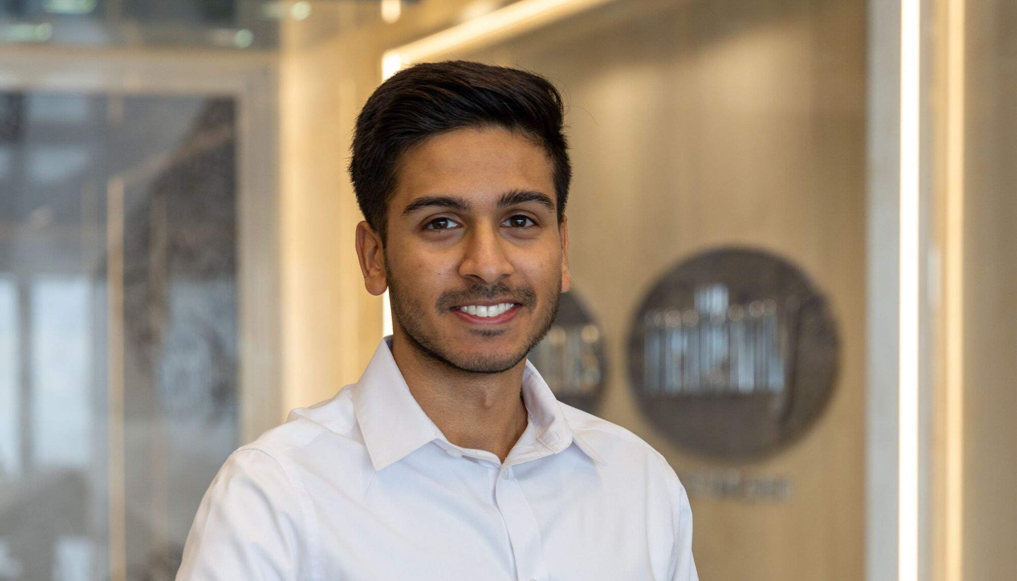 Male employee smiling at camera wearing white collared shirt in an office setting