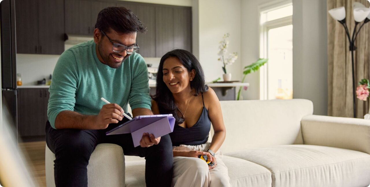 Man and woman sitting on couch in home looking at a tablet